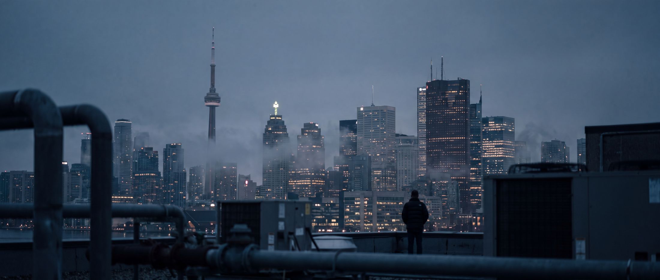 A lone figure on a rooftop looking out over the misty Toronto skyline