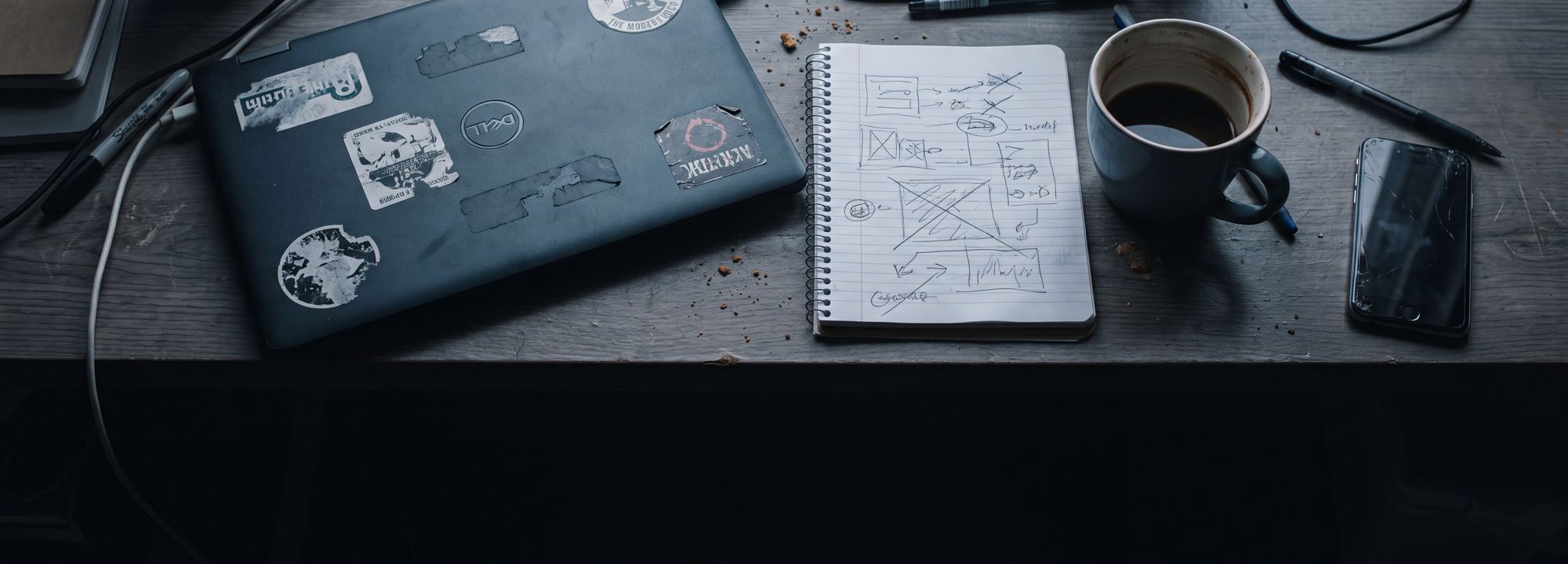 A worktable flat-lay: a laptop beside an open notebook of hand-drawn flow diagrams and a coffee